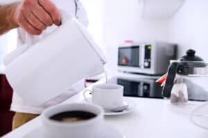 man preparing coffee, pouring hot water from electric kettle into prepared cups to represent the need for a home surge mitigator