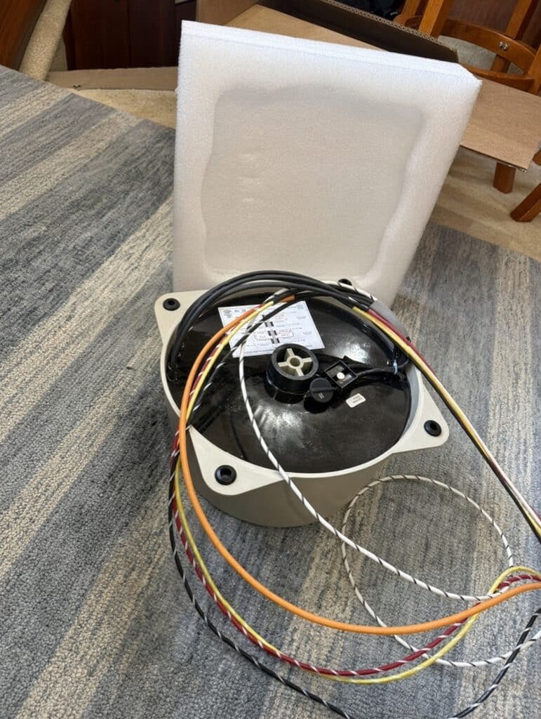 Marine-Puck MP6 marine isolation transformer unboxed on carpet, showing the sealed beige housing, black cover, nameplate, and color-coded shore-power leads beside its foam packing.